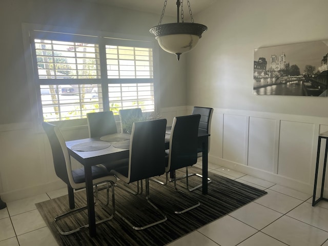 dining space featuring light tile patterned floors, a decorative wall, and a wainscoted wall