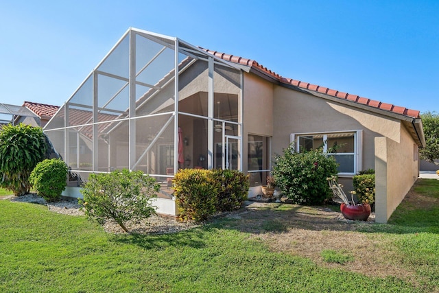 rear view of property with stucco siding, a lawn, glass enclosure, and a tile roof