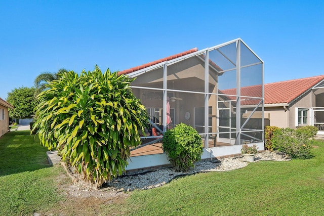 rear view of house with a tile roof, stucco siding, a lawn, and a lanai