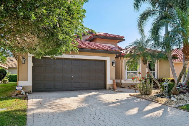 mediterranean / spanish home featuring stucco siding, an attached garage, a tile roof, and decorative driveway