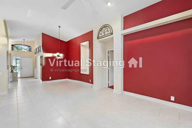 empty room with light tile patterned floors, ceiling fan with notable chandelier, and baseboards