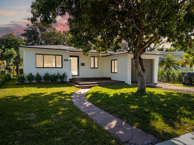 ranch-style house featuring covered porch, stucco siding, and a lawn