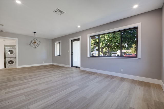 unfurnished living room featuring light wood-style floors, visible vents, baseboards, and stacked washer and dryer