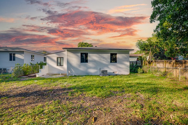 back of house at dusk featuring stucco siding, a lawn, and a fenced backyard