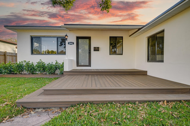 entrance to property featuring a wooden deck, fence, and stucco siding