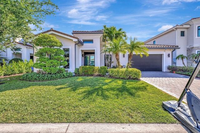 view of front of property with a tile roof, a front yard, stucco siding, decorative driveway, and an attached garage