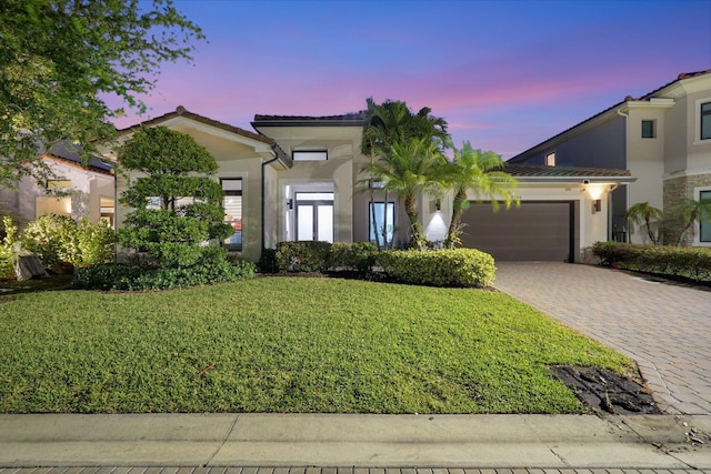 view of front of home with a front yard, an attached garage, stucco siding, a tile roof, and decorative driveway