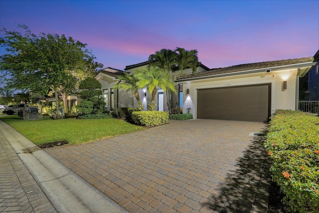 mediterranean / spanish home featuring an attached garage, stucco siding, a front lawn, a tiled roof, and decorative driveway