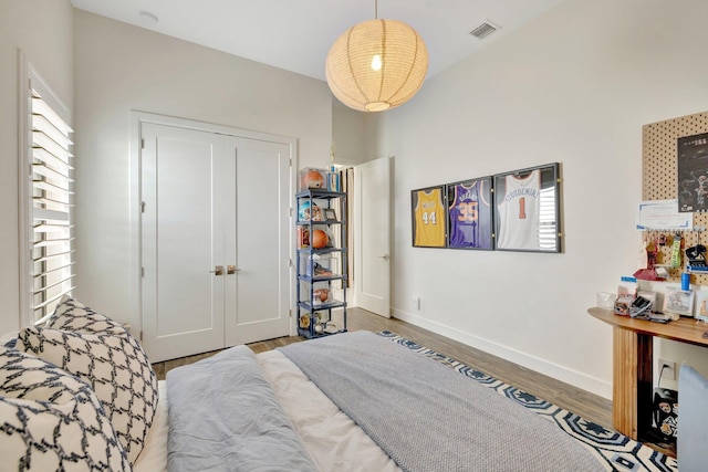 bedroom with a closet, baseboards, visible vents, and wood finished floors