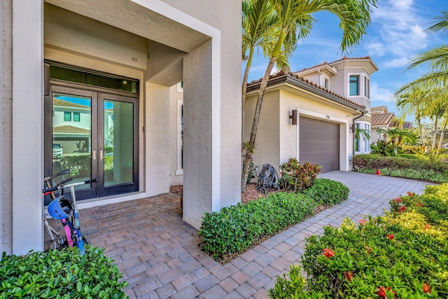 view of exterior entry with decorative driveway, french doors, a garage, and stucco siding