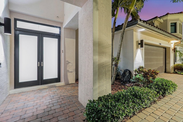 property entrance with french doors, driveway, an attached garage, and stucco siding