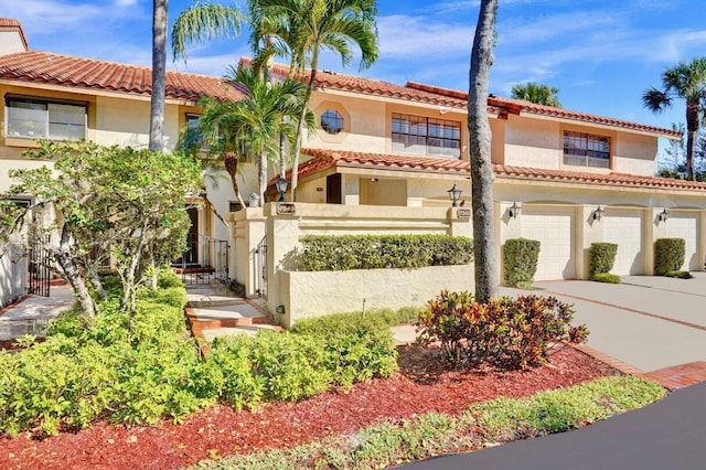 mediterranean / spanish-style house with stucco siding, a tile roof, fence, concrete driveway, and an attached garage