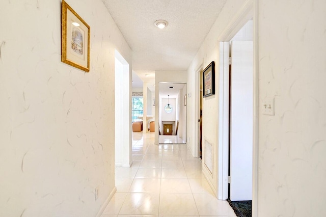 hallway with light tile patterned floors, baseboards, visible vents, a textured ceiling, and a textured wall