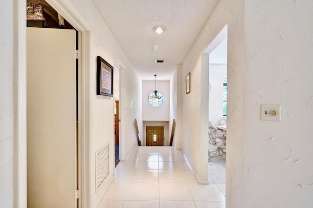 hall featuring visible vents, an upstairs landing, a textured ceiling, and light tile patterned flooring