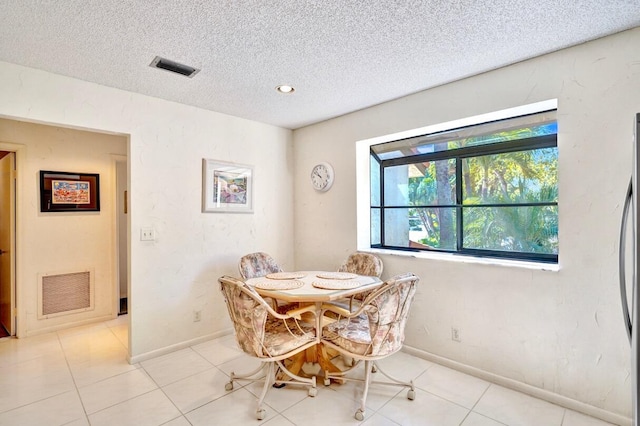 dining area featuring light tile patterned floors, visible vents, a textured ceiling, and baseboards