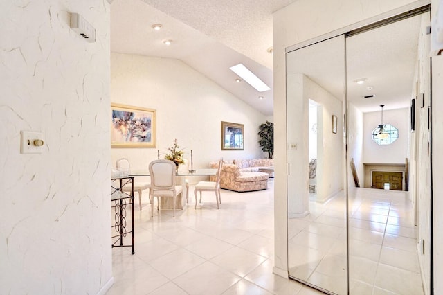 hall with vaulted ceiling with skylight, a textured ceiling, and light tile patterned flooring