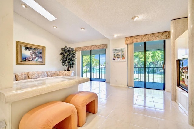 interior space with baseboards, recessed lighting, vaulted ceiling with skylight, light tile patterned flooring, and a textured ceiling