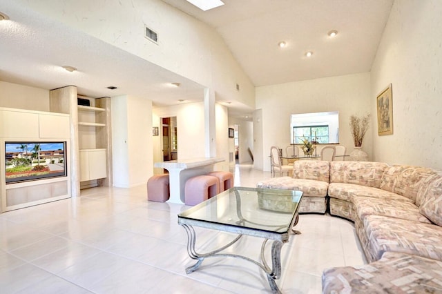 living room featuring light tile patterned floors, visible vents, vaulted ceiling with skylight, and a textured ceiling