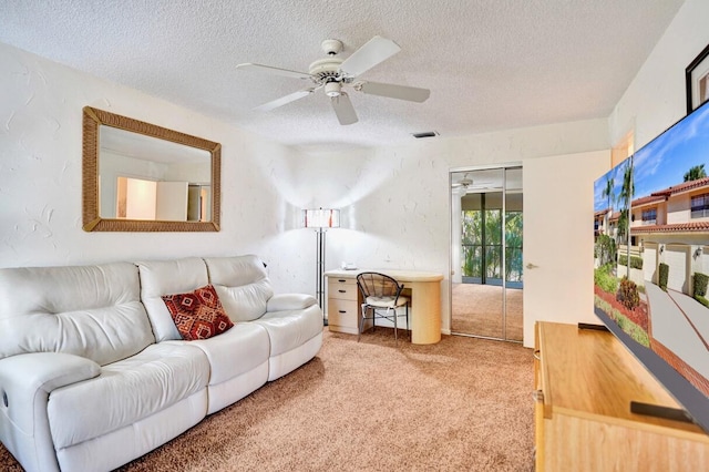 carpeted living area with ceiling fan, a textured wall, visible vents, and a textured ceiling