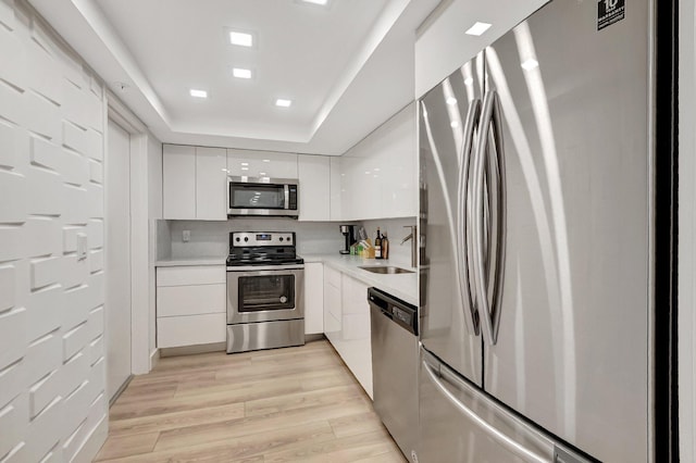 kitchen featuring light wood-style flooring, appliances with stainless steel finishes, white cabinets, modern cabinets, and a sink