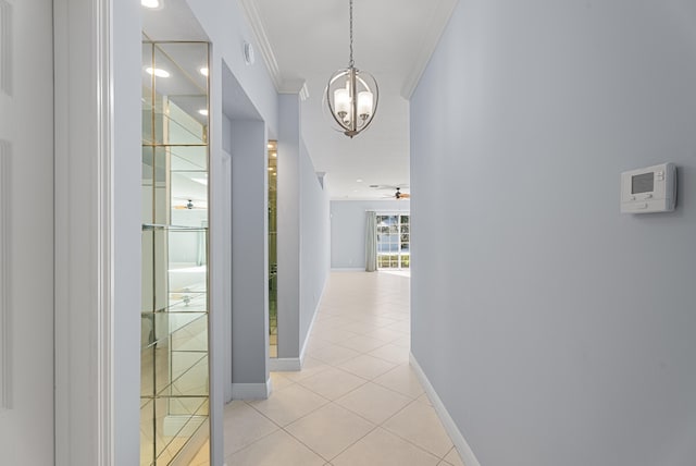 hallway featuring light tile patterned flooring, baseboards, an inviting chandelier, and ornamental molding