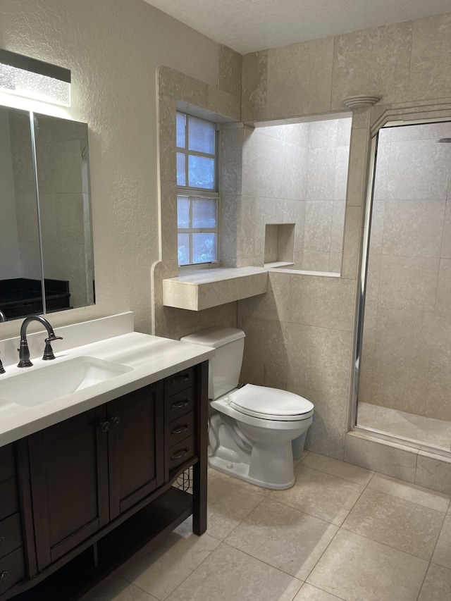 bathroom featuring tile patterned floors, toilet, a walk in shower, vanity, and a textured wall