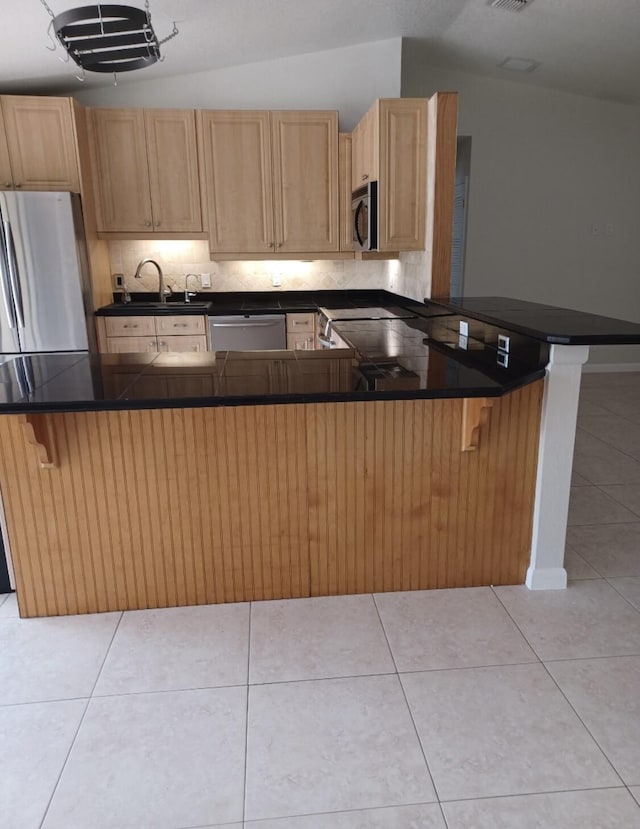 kitchen with a sink, dark countertops, appliances with stainless steel finishes, and light tile patterned flooring