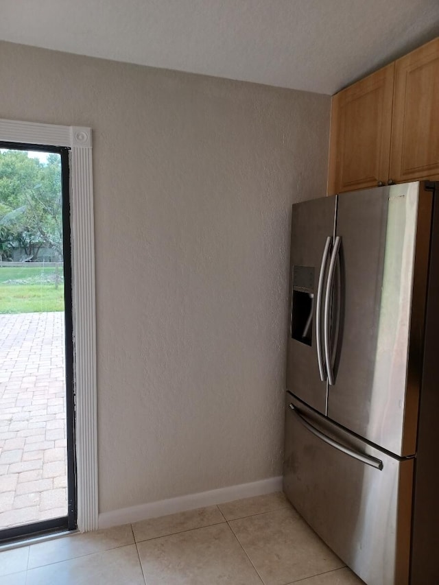 kitchen featuring light tile patterned flooring, baseboards, stainless steel refrigerator with ice dispenser, and a textured wall