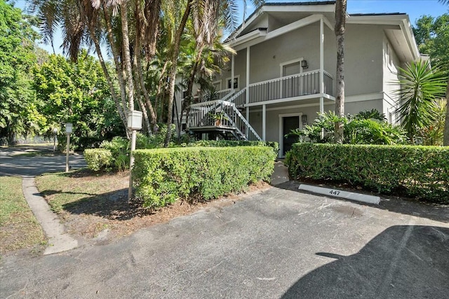 view of front facade featuring stucco siding, uncovered parking, and stairway