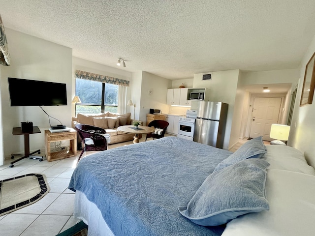 bedroom with light tile patterned flooring, visible vents, a textured ceiling, and freestanding refrigerator