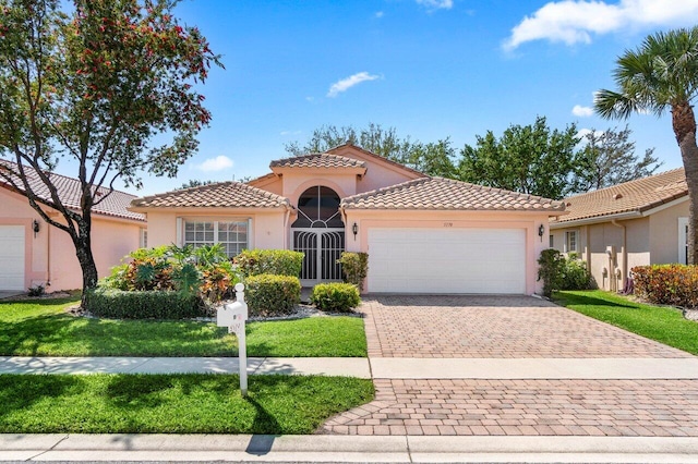 mediterranean / spanish-style home with stucco siding, a tiled roof, decorative driveway, and a garage