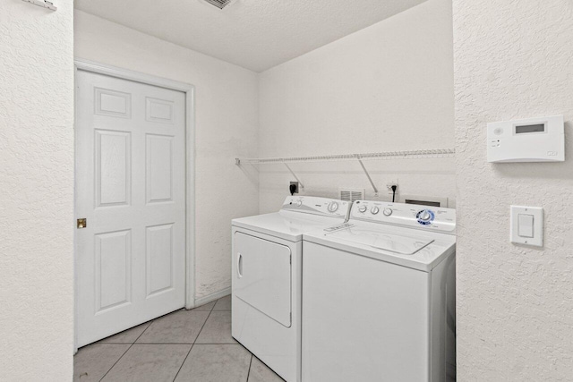 washroom with laundry area, light tile patterned floors, washing machine and dryer, and a textured wall