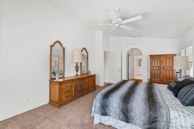 carpeted bedroom featuring a ceiling fan, ensuite bathroom, a textured ceiling, arched walkways, and lofted ceiling