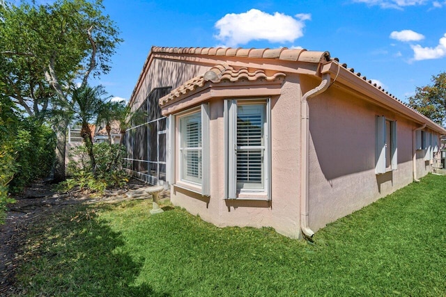 view of property exterior featuring stucco siding, glass enclosure, and a yard