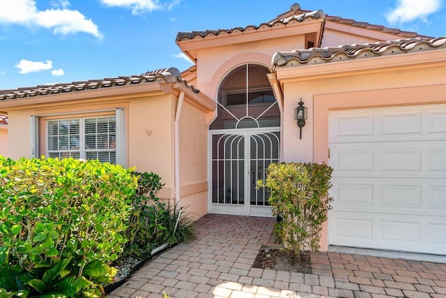 view of exterior entry with stucco siding, driveway, a gate, a garage, and a tiled roof