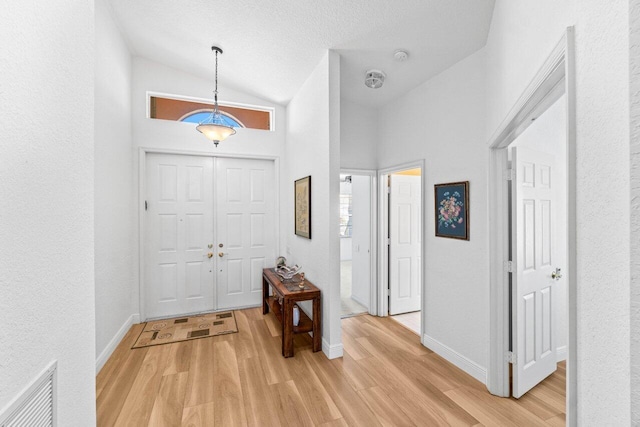 foyer featuring baseboards, light wood-type flooring, lofted ceiling, and visible vents