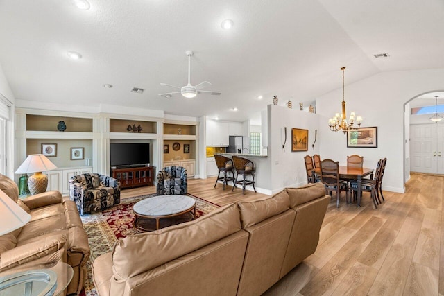 living area with visible vents, built in features, light wood-type flooring, vaulted ceiling, and ceiling fan with notable chandelier