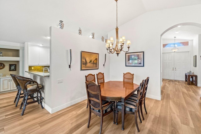 dining space featuring baseboards, vaulted ceiling, an inviting chandelier, light wood-style floors, and arched walkways