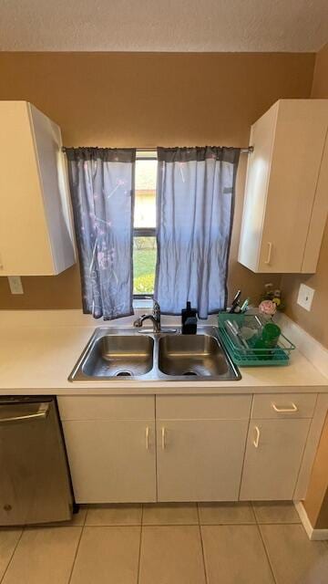 kitchen with stainless steel dishwasher, light countertops, a sink, and light tile patterned floors