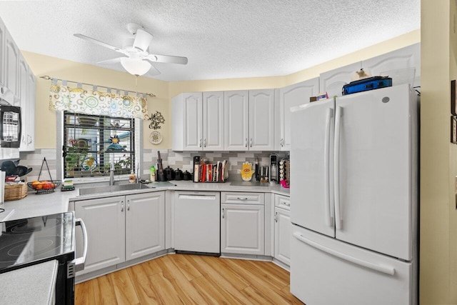 kitchen featuring light wood finished floors, white appliances, light countertops, and a sink