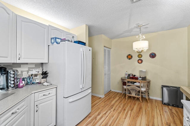 kitchen with decorative light fixtures, light wood-type flooring, light countertops, freestanding refrigerator, and white cabinets