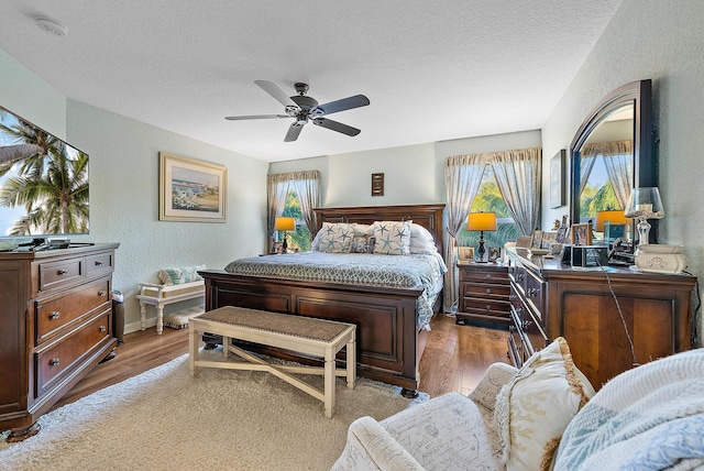 bedroom featuring a ceiling fan, wood finished floors, a textured wall, and a textured ceiling