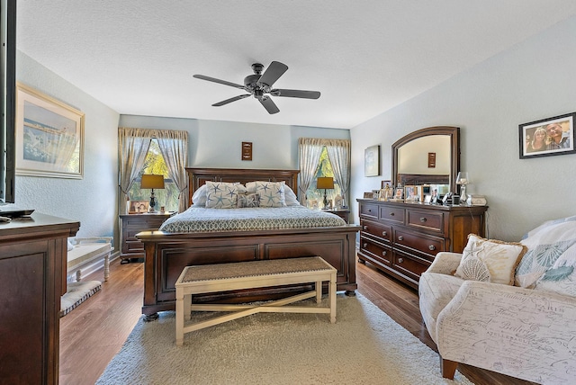 bedroom with ceiling fan, light wood-style flooring, and a textured wall