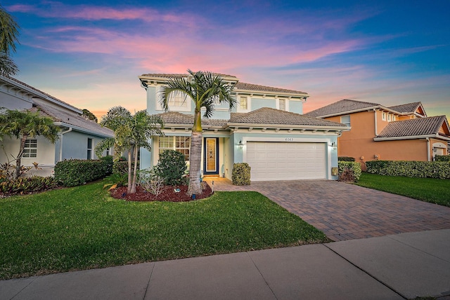 mediterranean / spanish home with a tiled roof, stucco siding, a lawn, decorative driveway, and an attached garage