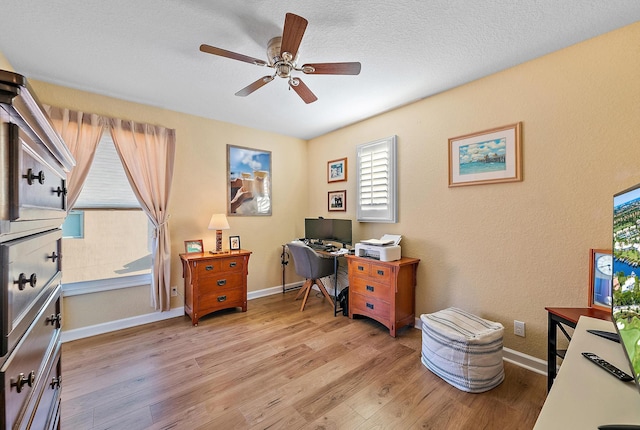 office space with light wood-style flooring, a textured ceiling, baseboards, and ceiling fan