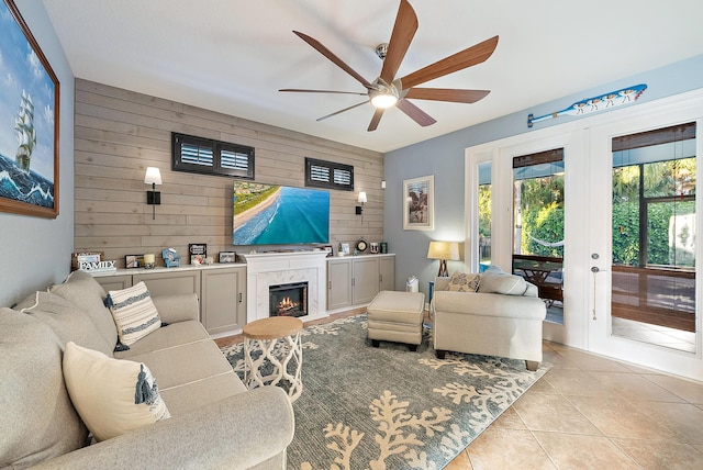 living room featuring wooden walls, light tile patterned floors, a premium fireplace, ceiling fan, and french doors