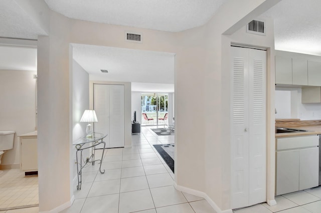 corridor with light tile patterned floors, visible vents, and a textured ceiling