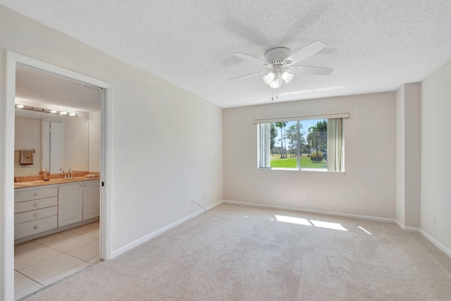 unfurnished bedroom featuring a ceiling fan, baseboards, ensuite bathroom, a textured ceiling, and light colored carpet