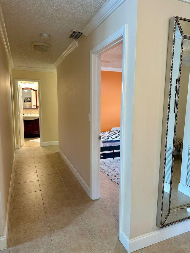 hall featuring crown molding, light tile patterned floors, visible vents, and a textured ceiling