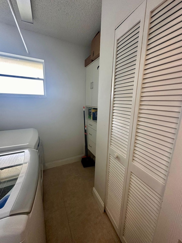 clothes washing area featuring baseboards, washer and dryer, tile patterned floors, cabinet space, and a textured ceiling